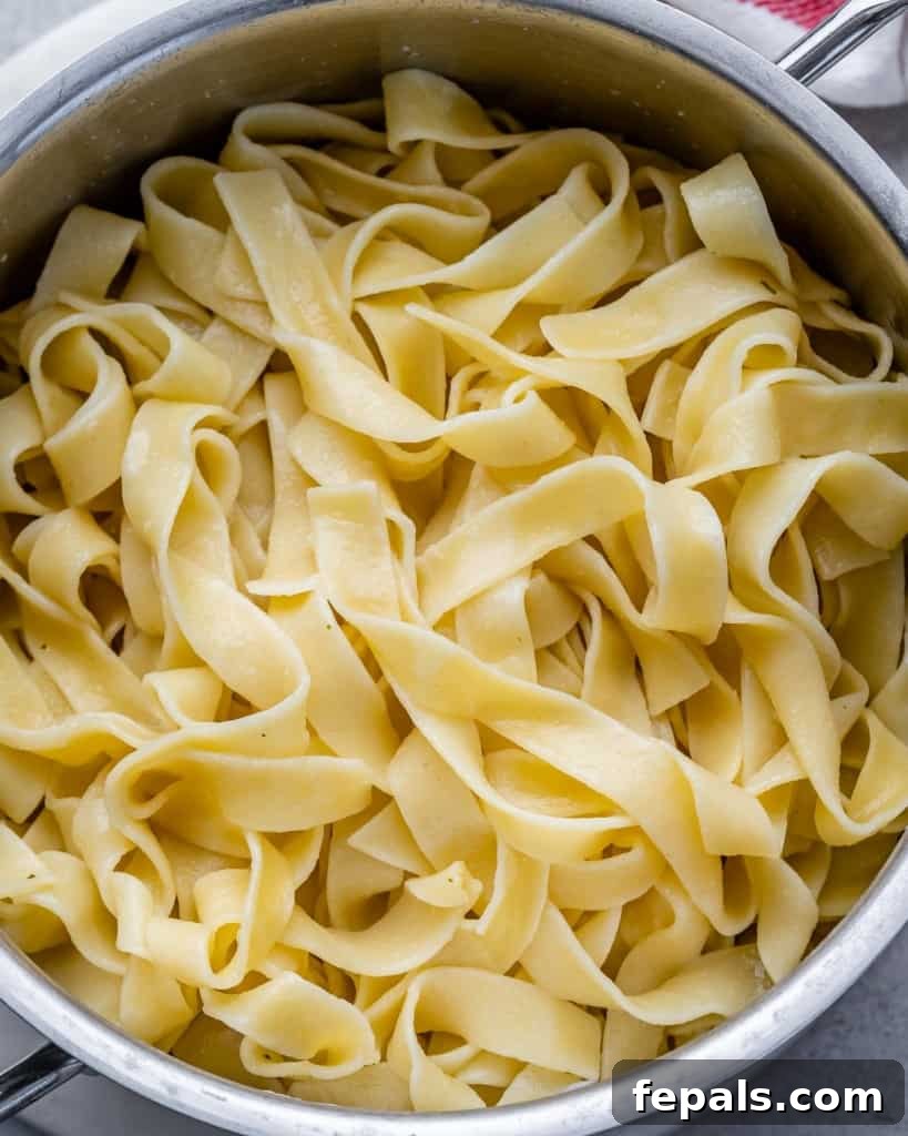 Close-up of perfectly cooked fettuccine pasta being drained in a pot, with steam rising.