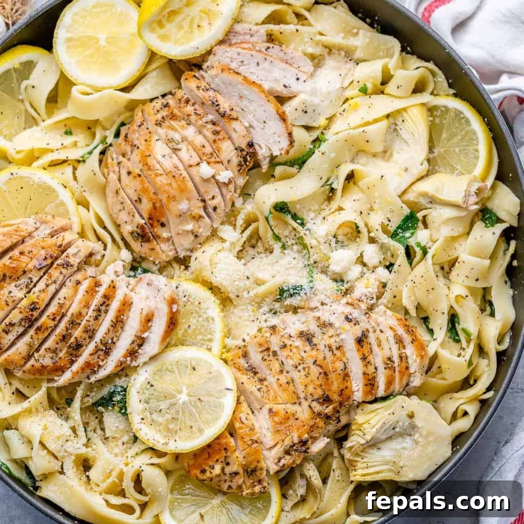 A close-up, top-down view of a serving of lemon garlic chicken pasta, garnished with fresh lemon slices and parsley, showcasing the creamy sauce and tender chicken.