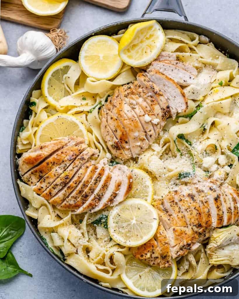 Top view of a full skillet of lemon garlic chicken pasta, garnished with fresh herbs and lemon slices, ready to be served.