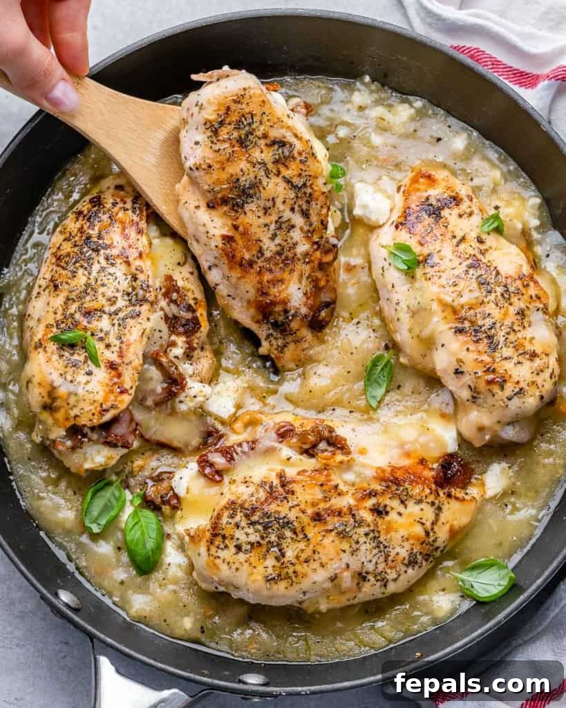 Savory Sun-dried Tomatoes and Cheese Stuffed Chicken 2 Top view image of 4 golden brown stuffed chicken breasts nestled in a black skillet with a rich sauce, ready to be served by a wooden spoon.