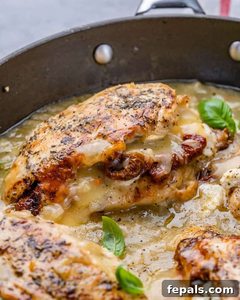 Savory Sun-dried Tomatoes and Cheese Stuffed Chicken 7 Side shot and close up view of a luscious stuffed chicken breast with melted cheese and tomatoes in a black pan, perfectly cooked and glistening with sauce.