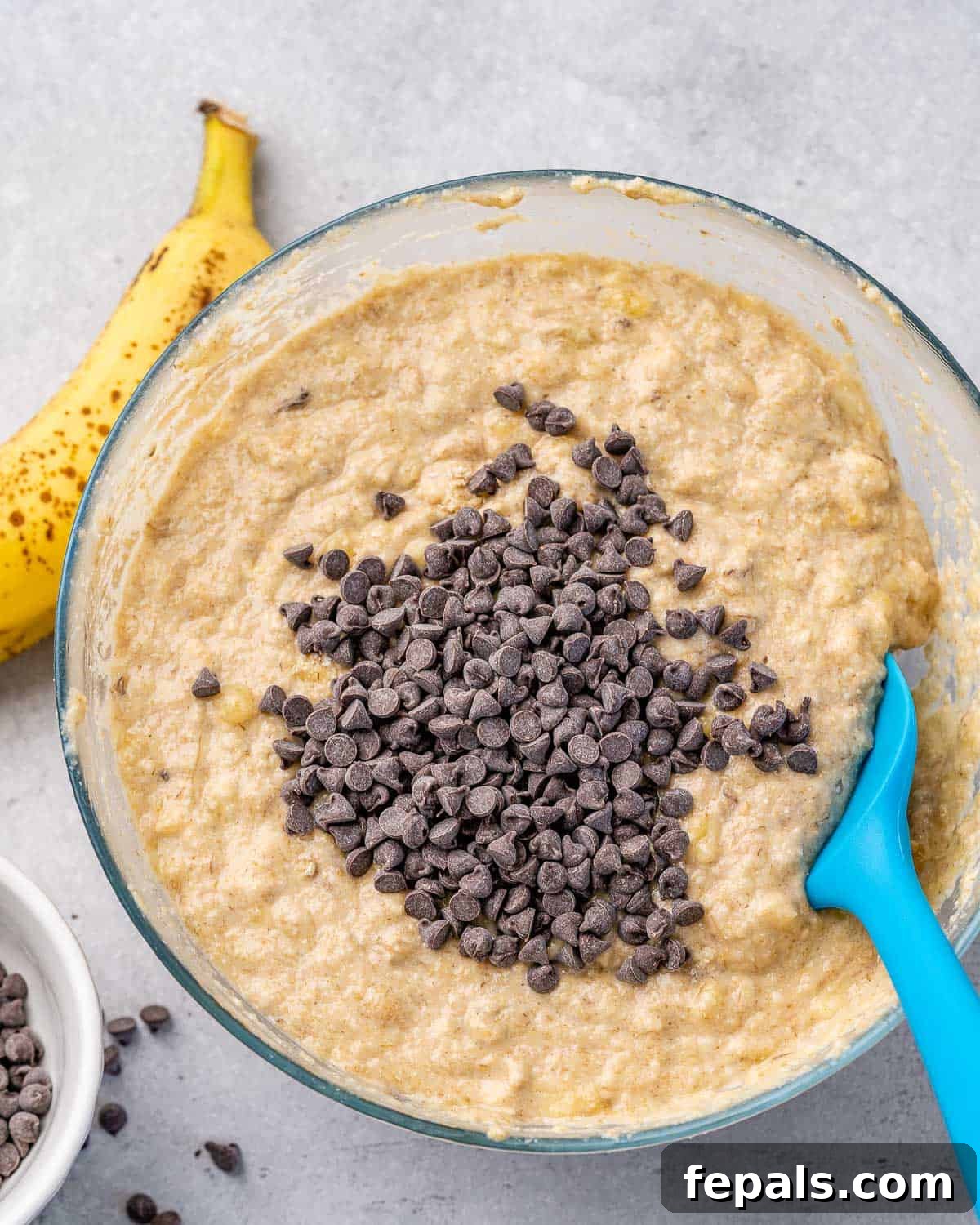 Close-up of vegan banana bread batter in a mixing bowl, generously studded with dairy-free chocolate chips, ready for baking.