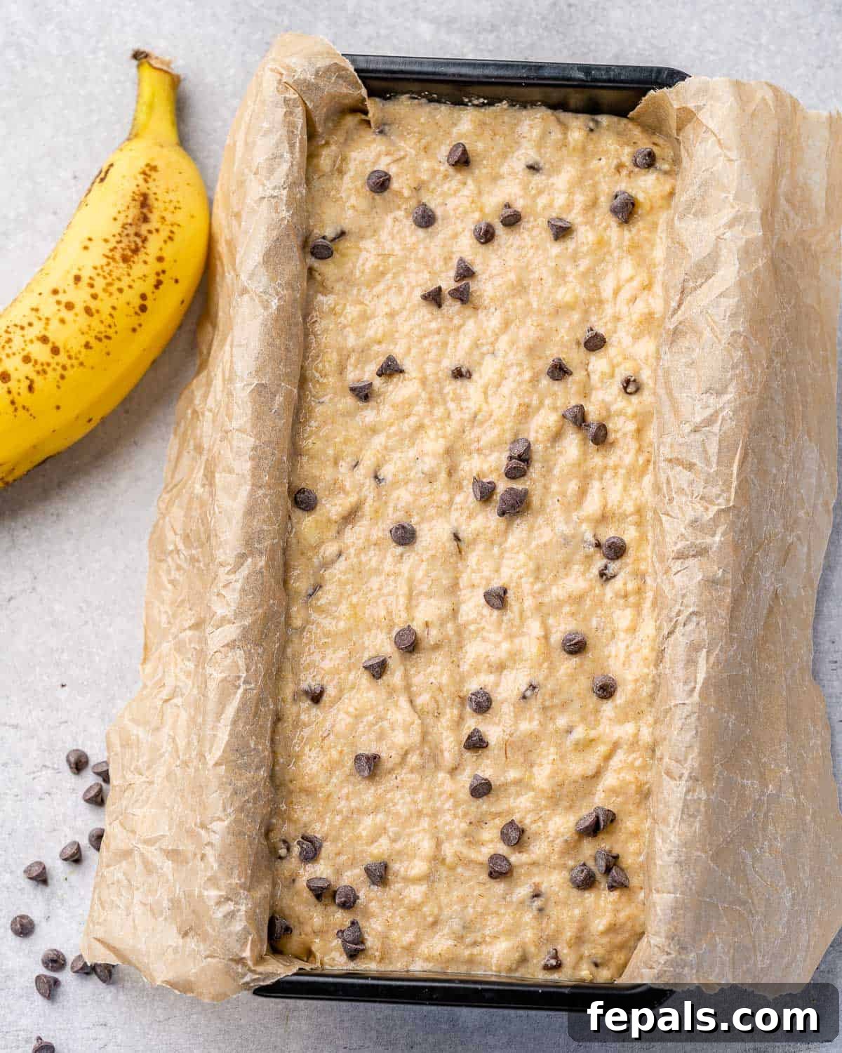Vegan banana bread batter poured into a parchment-lined loaf pan, adorned with chocolate chips on top, ready for the oven.