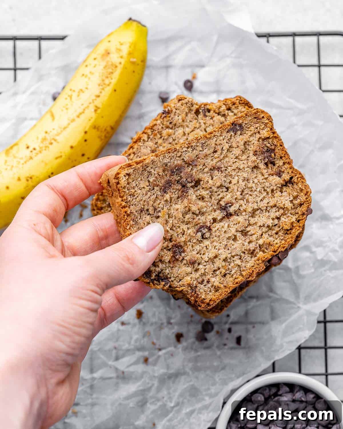 Close-up of a hand holding a single, perfectly sliced piece of moist vegan banana bread, highlighting its texture and deliciousness.