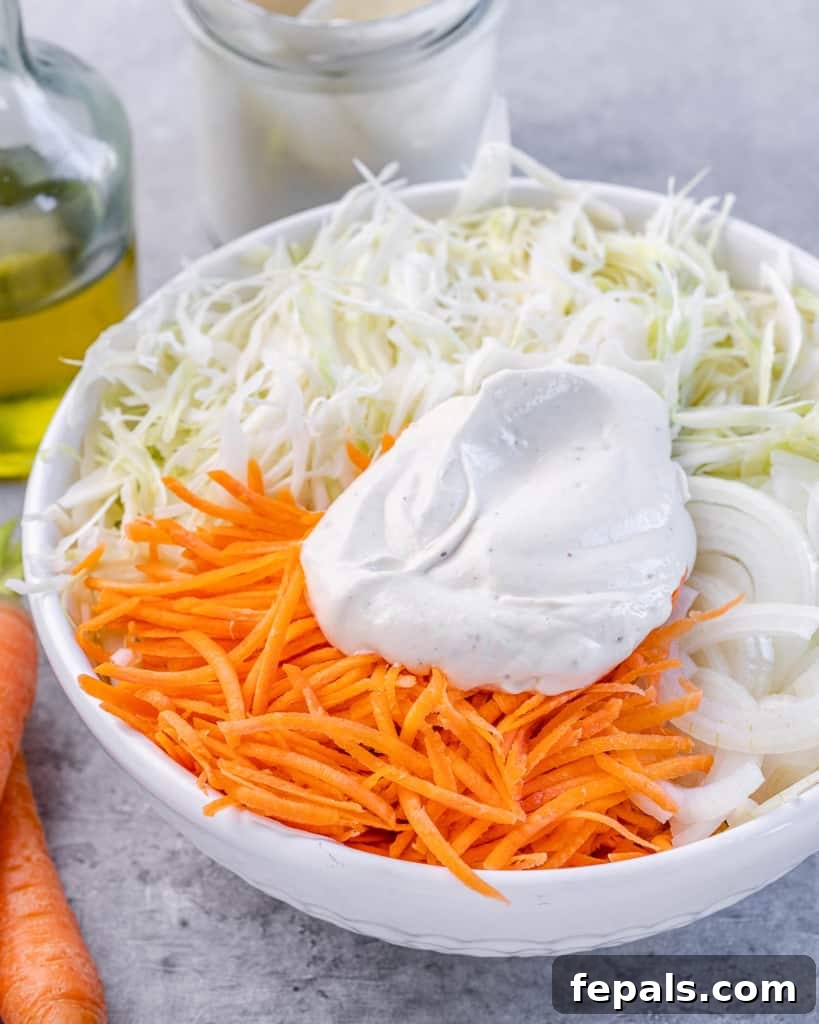 Wholesome Homemade Coleslaw 6 yogurt dressing dollop over the shredded carrots and cabbage in a white bowl before tossing together