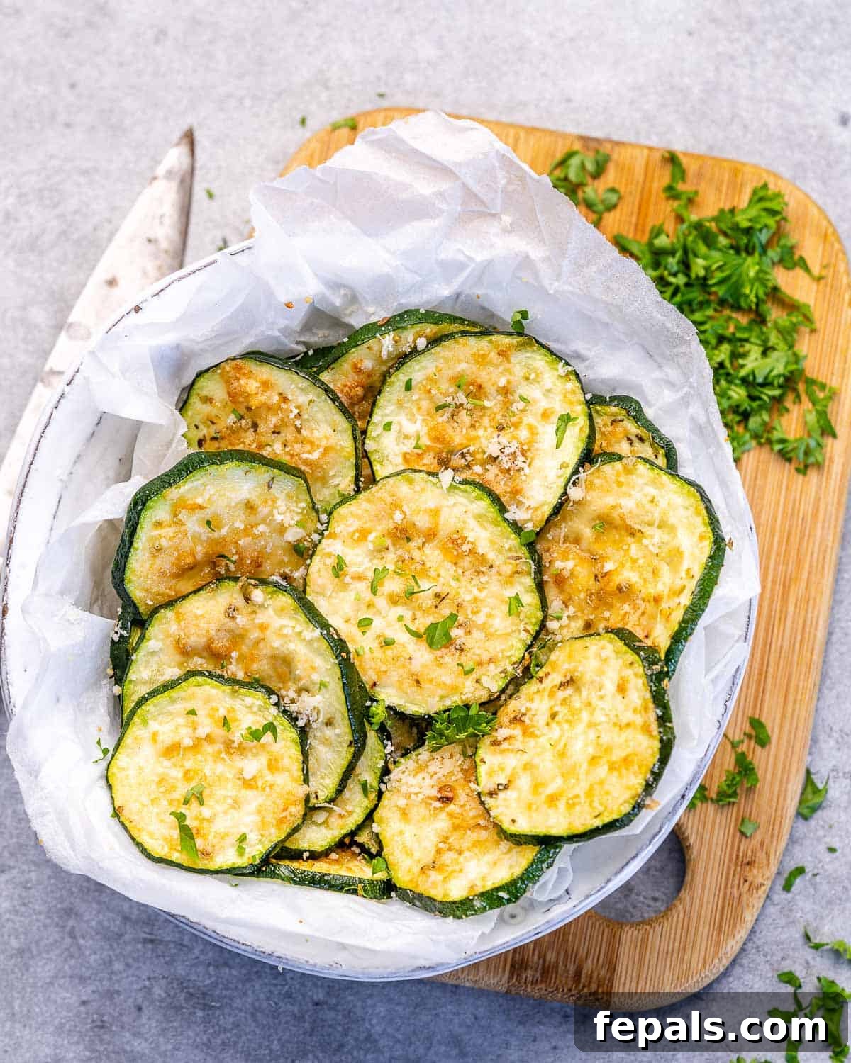 Baked Zucchini Chips baked sliced zucchini in a bowl on a brown cutting board