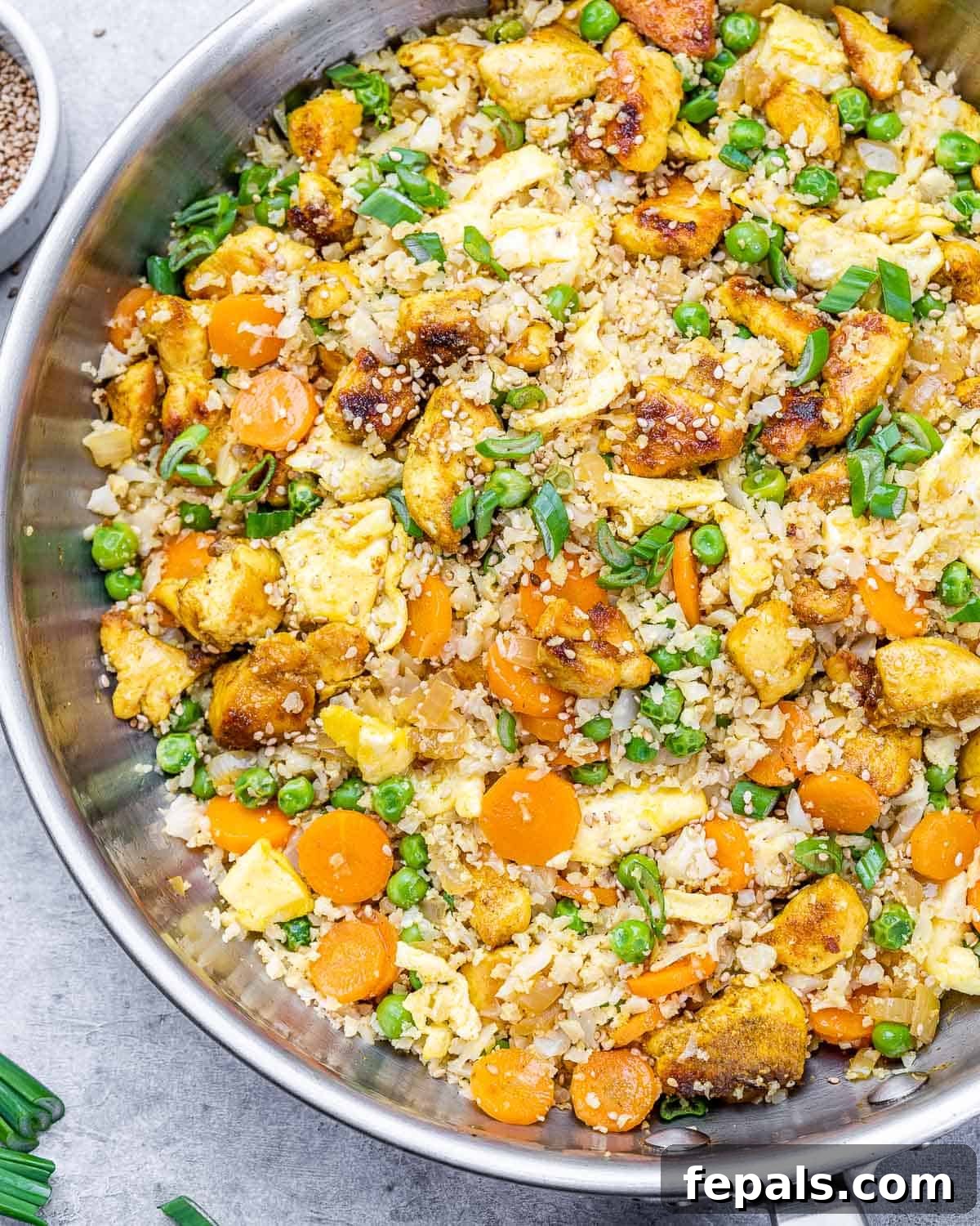 Skillet with tender chicken and healthy cauliflower fried rice ingredients including carrots and green onions