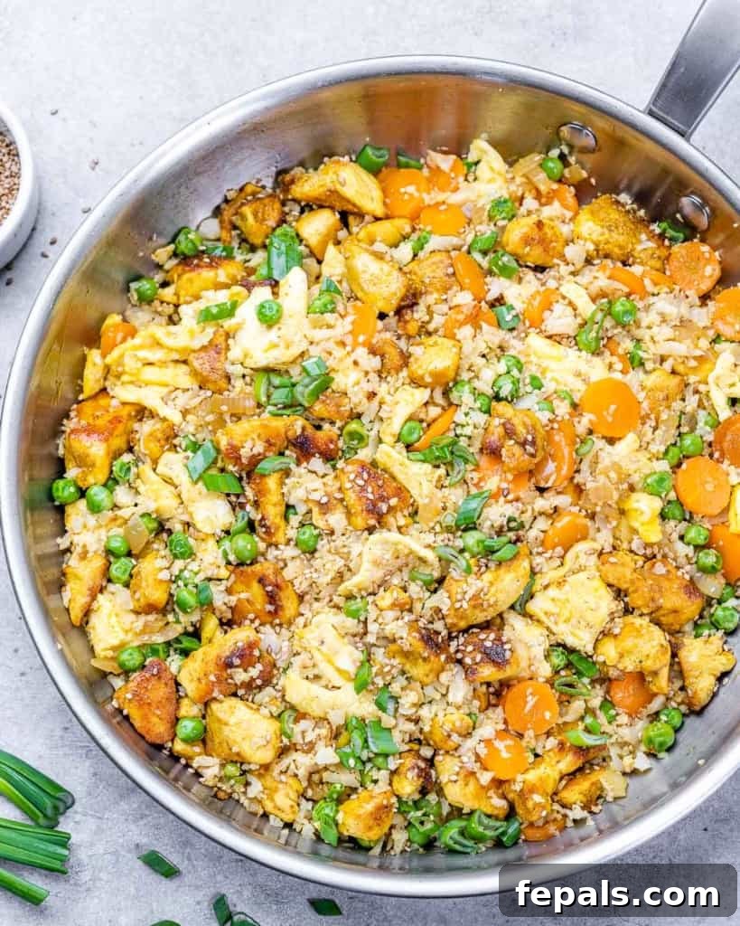 Top view of cauliflower fried rice in a silver stainless steel pan, beautifully garnished