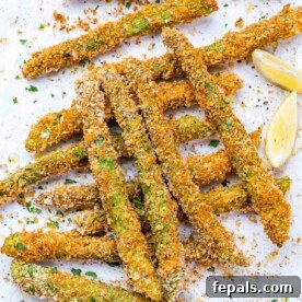 Crispy oven baked asparagus on white baking sheet with lemon wedge garnish.