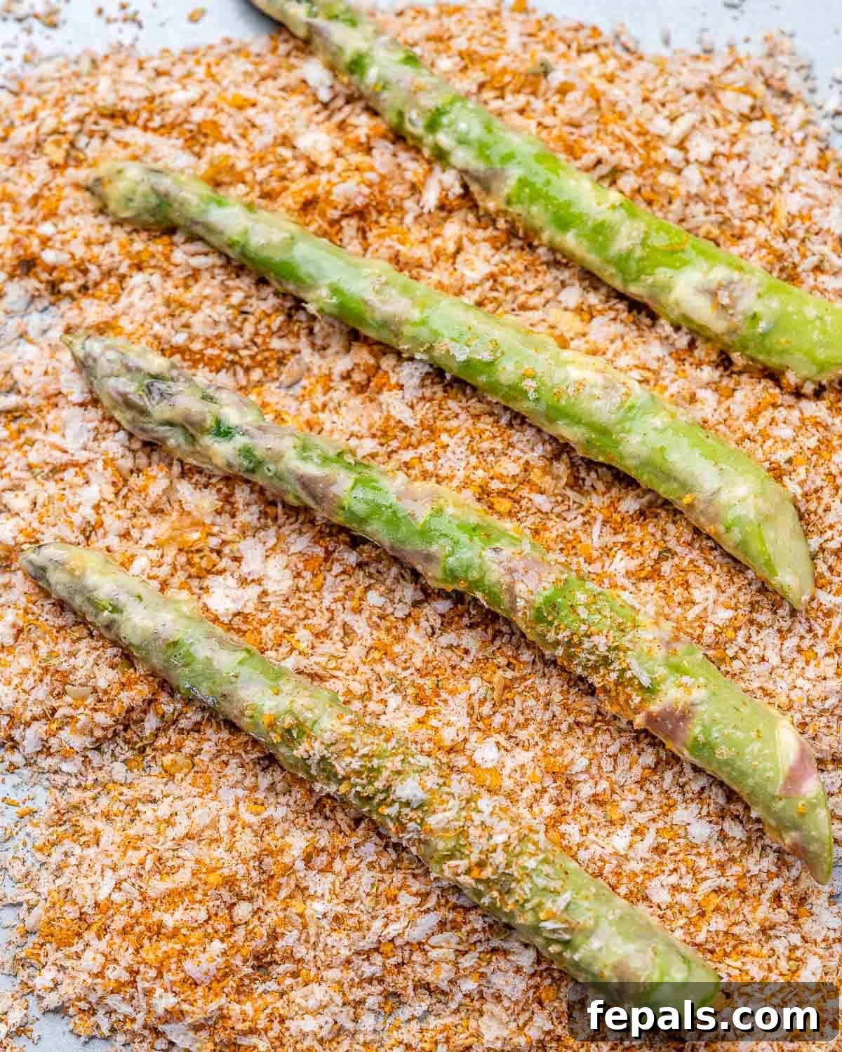 Asparagus getting evenly coated in breadcrumb mixture.
