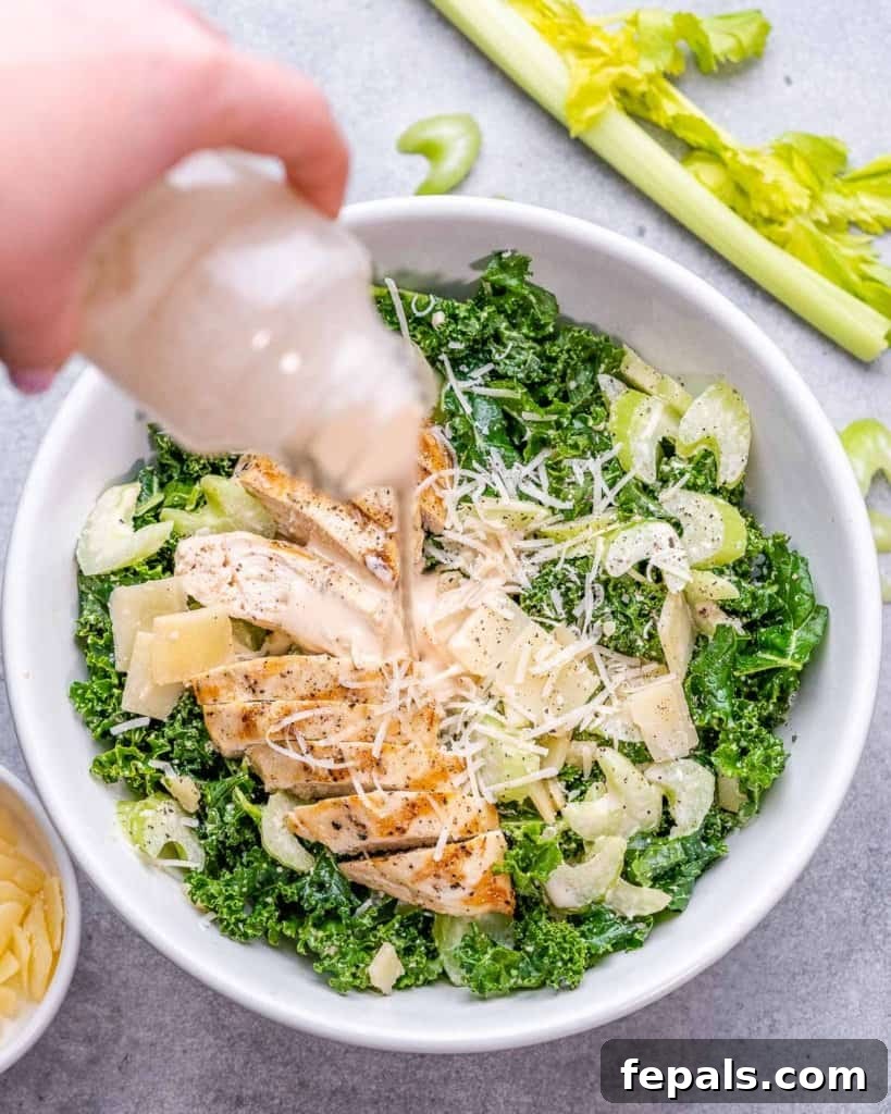 Flame-Kissed Chicken Kale Caesar 7 salad dressing in a bottle being poured over chicken kale salad in a white bowl