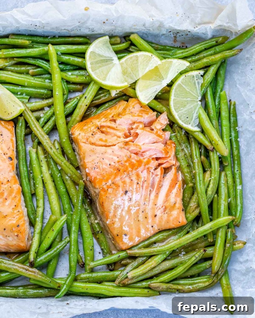 baked salmon filet on pan with green beans and lime garnishes