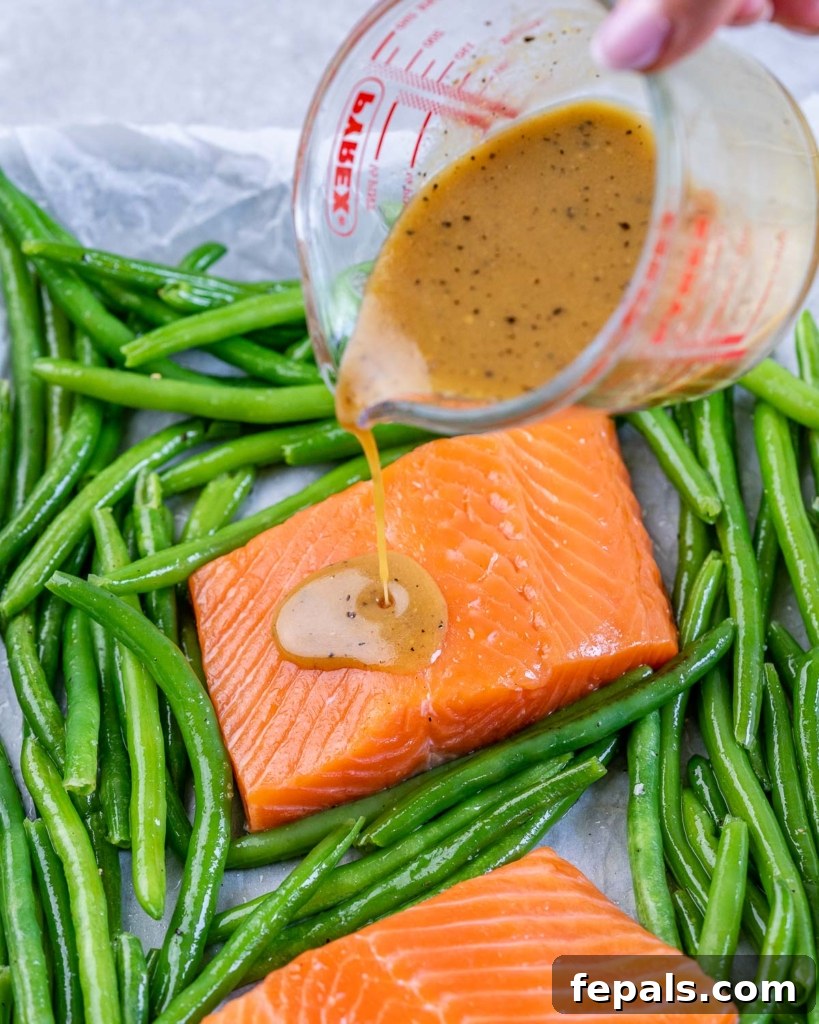 pouring maple glaze over salmon on the pan with green beans around it 