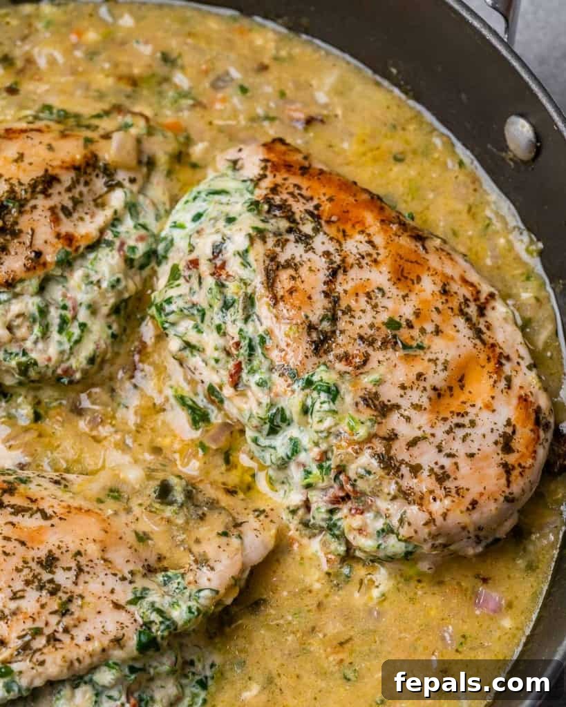 Tuscan Cheese-Stuffed Chicken 3 Close-up view of a succulent Italian stuffed chicken breast, sliced to reveal its creamy, spinach, and cheese filling, resting on a bed of sauce