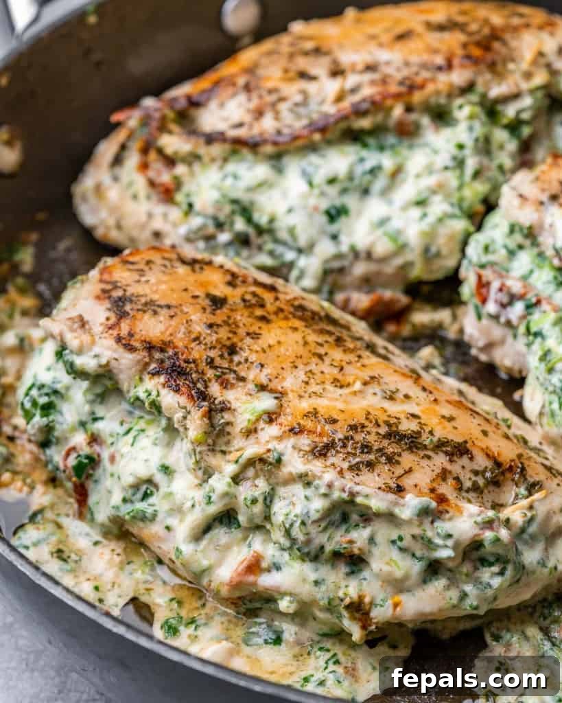 Tuscan Cheese-Stuffed Chicken 7 A side view of golden-brown Italian stuffed chicken breasts simmering in a rich, creamy sauce within a black skillet on the stovetop.