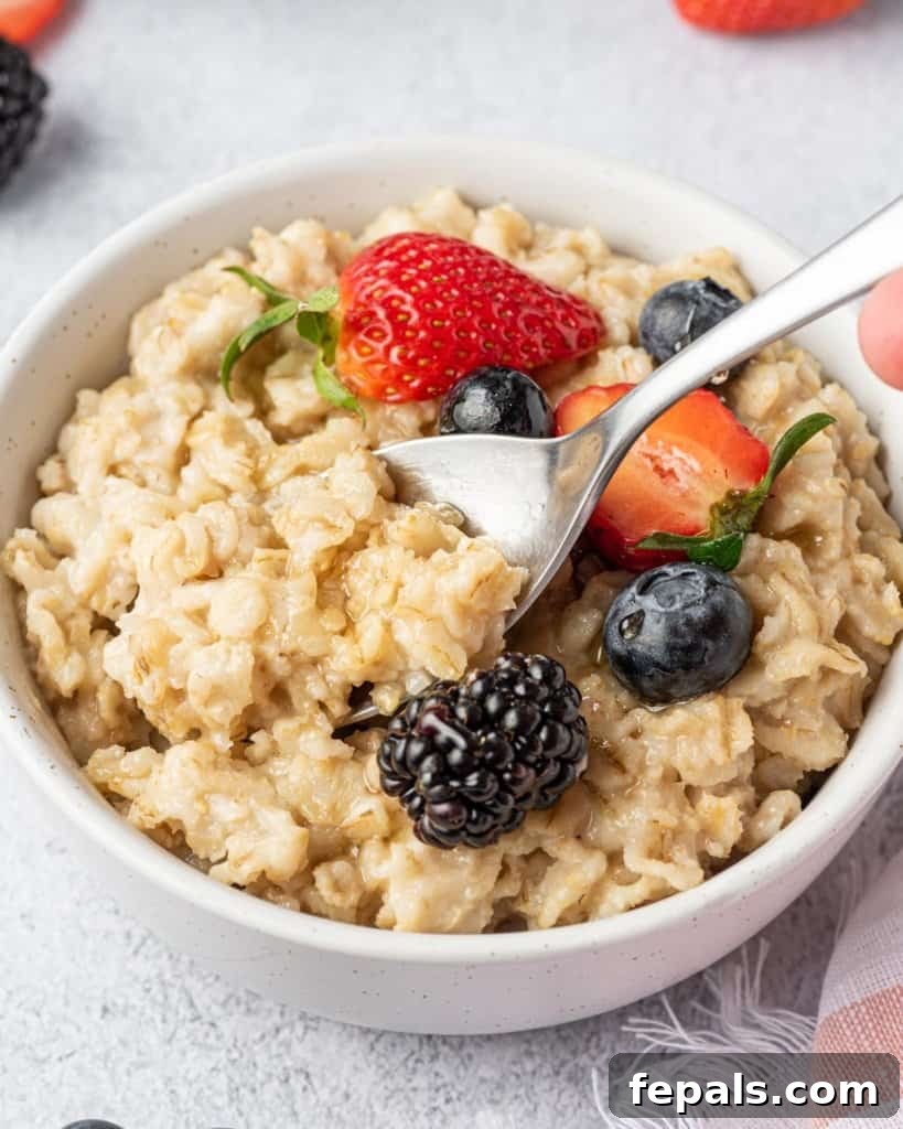 Effortless Instant Pot Oatmeal 2 side shot of an oatmeal bowl with a spoon in it, topped with berries and maple syrup