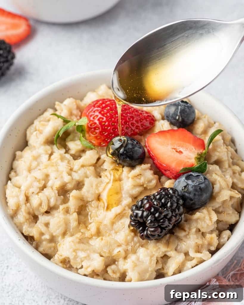 Effortless Instant Pot Oatmeal 3 maple syrup being added over a bowl of oatmeal topped with berries