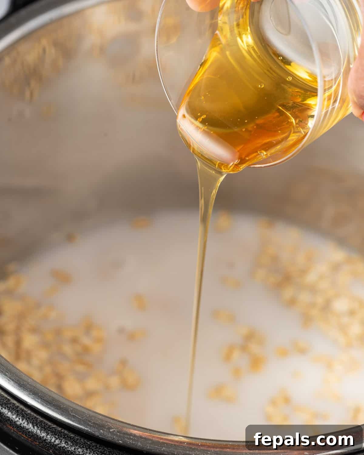 Effortless Instant Pot Oatmeal 6 maple syrup being poured into the instant pot that already has oats and milk in it.