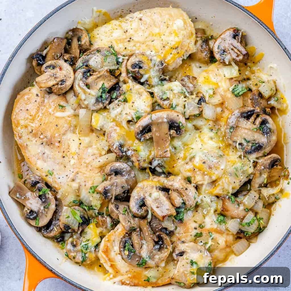 tope view of chicken breast satuteed with mushroom and topped with cheese over an orange skillet