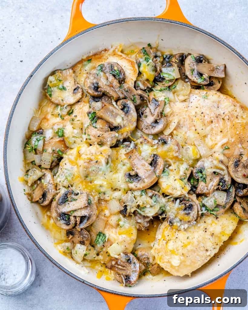 top view chicken and mushroom in an orange skillet topped with cheesee