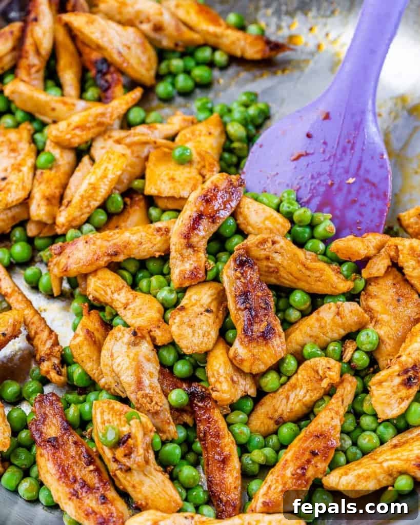 Lighter Chicken Carbonara 5 Cooked chicken and peas are sautéed together in a stainless steel pan, with a purple spatula resting in it.