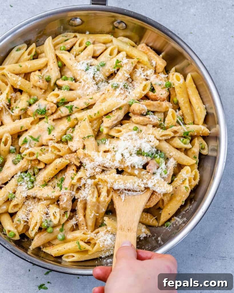 Lighter Chicken Carbonara 7 A hand is serving creamy chicken carbonara pasta from a stainless steel pan with a wooden spoon, ready to be enjoyed.