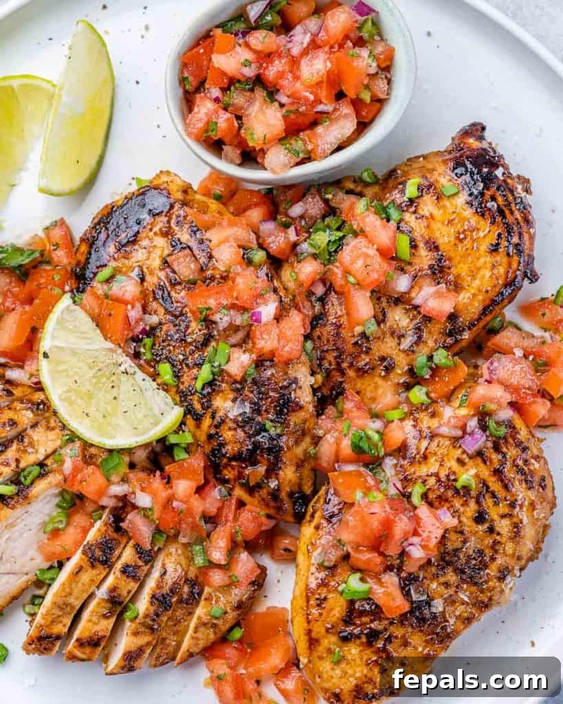 The Ultimate Jerk Chicken 7 Top view of grilled sliced chicken breast on a white plate with a generous side of vibrant tomato salsa, ready to be enjoyed.