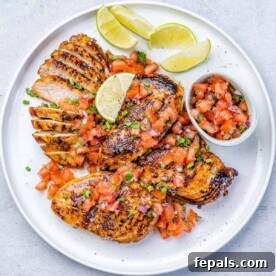 top view cooked jerk chicken breast on a plate with lime garnish and side of salsa
