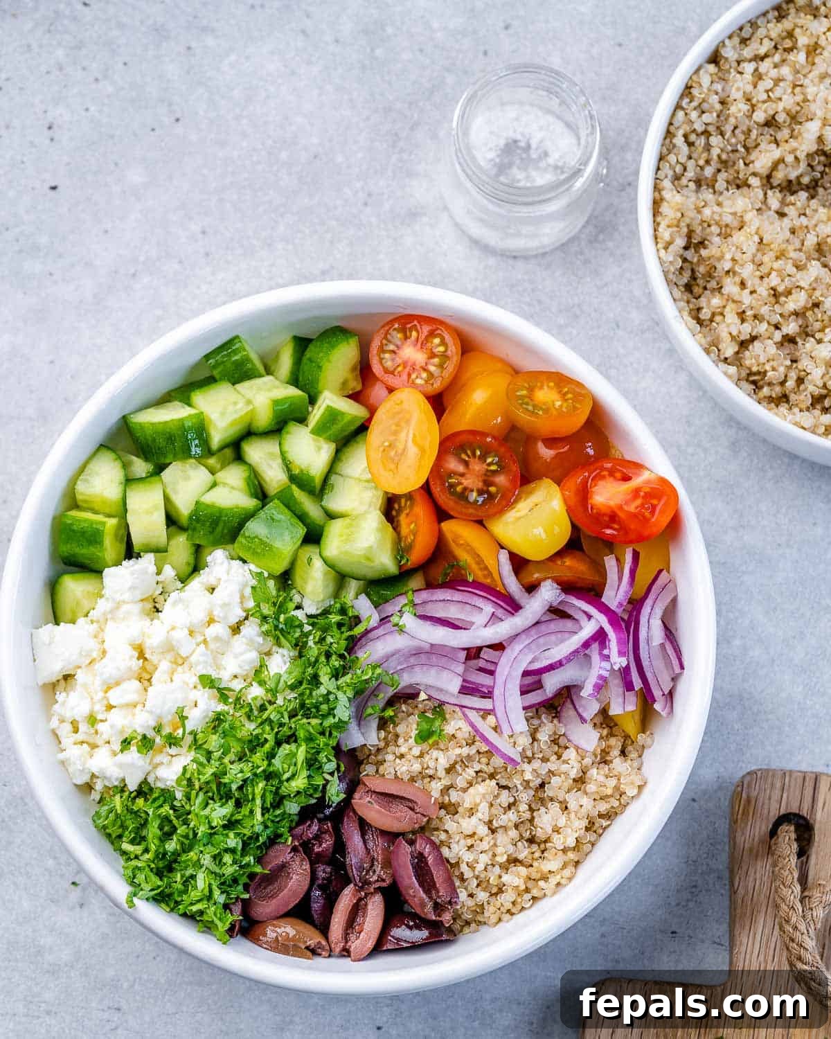 Vibrant Mediterranean Quinoa Salad 6 All prepped quinoa salad ingredients carefully arranged on top of the dressing in a circular white bowl.