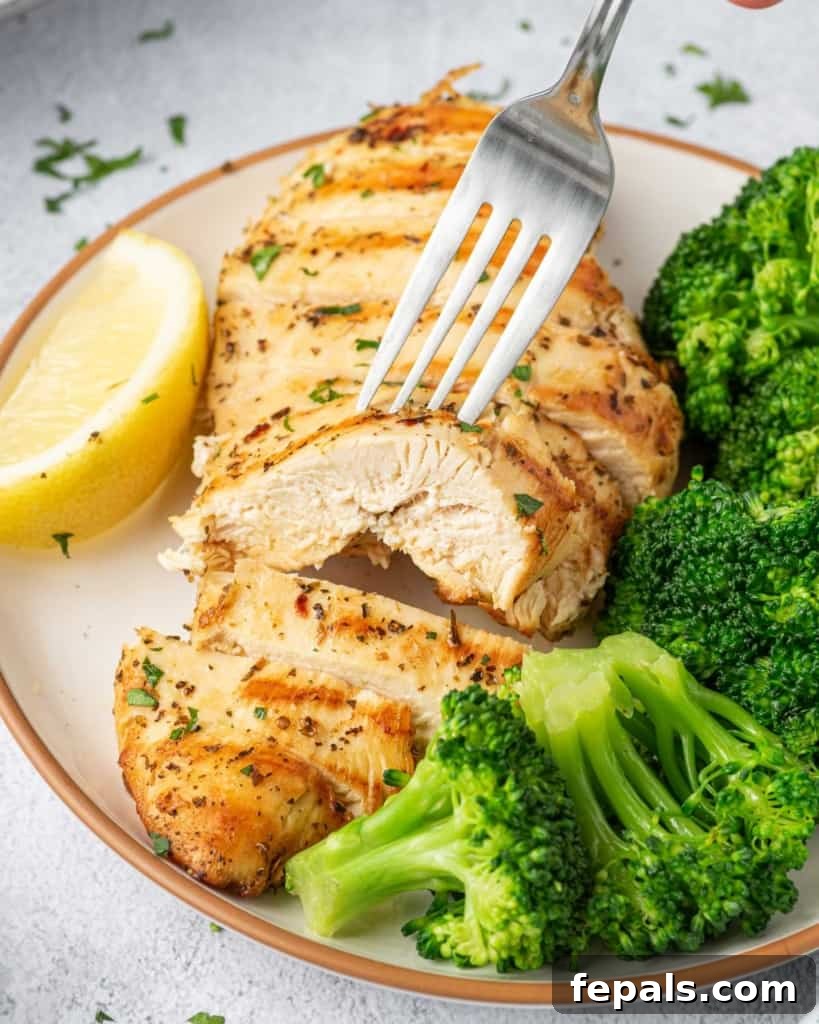 Juicy Italian Grilled Chicken Breasts 11 A fork piercing a succulent slice of Italian grilled chicken breast, positioned on a plate with fresh broccoli florets.
