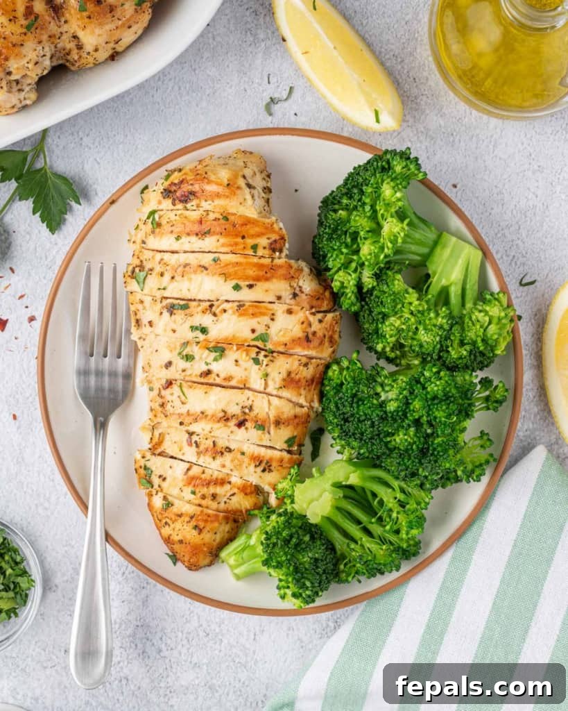 Juicy Italian Grilled Chicken Breasts 9 A grilled Italian chicken breast, thinly sliced, presented on a white plate with a side of vibrant green broccoli.