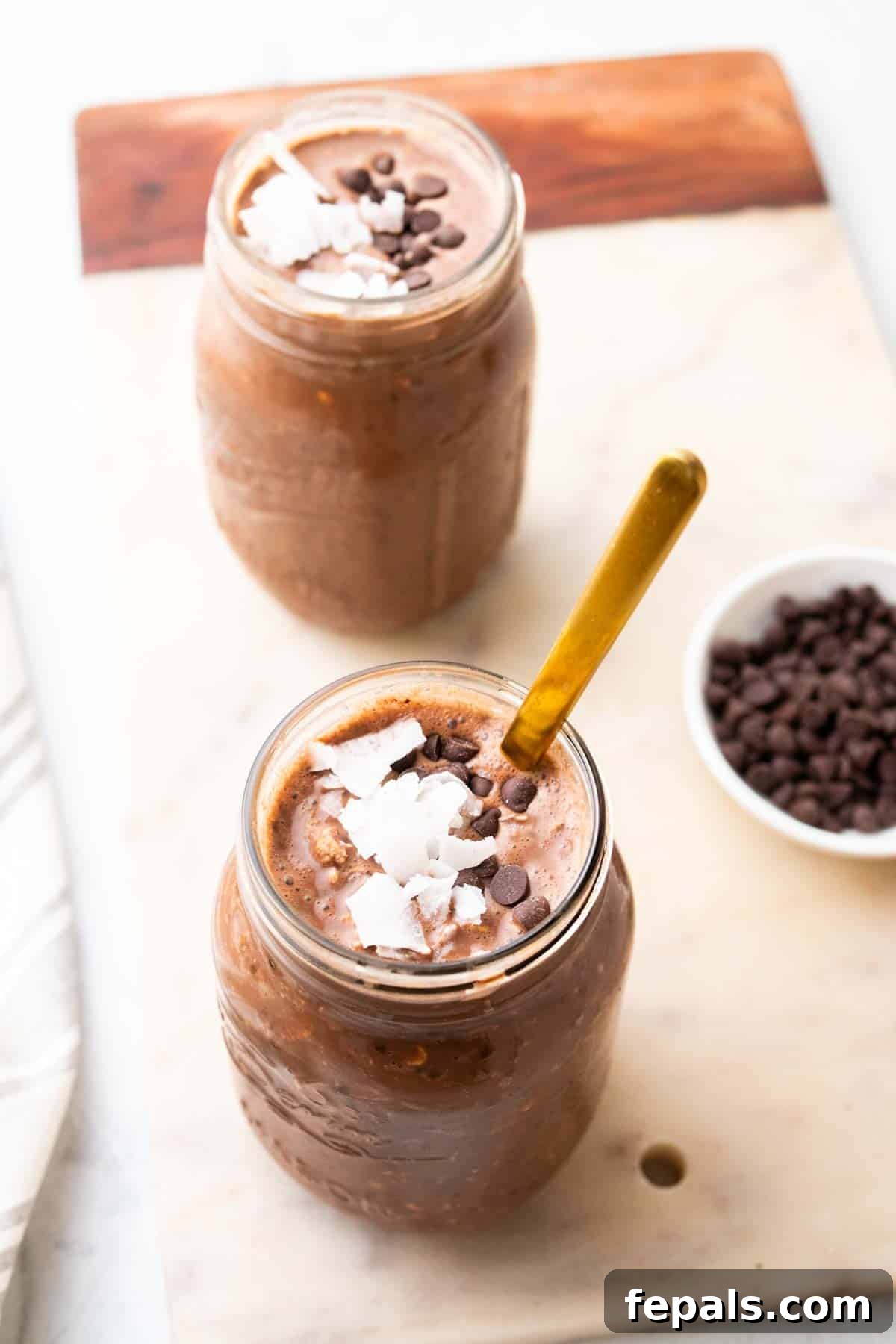 Two jars of chocolate peanut butter overnight oats with spoons and chocolate chips for garnish