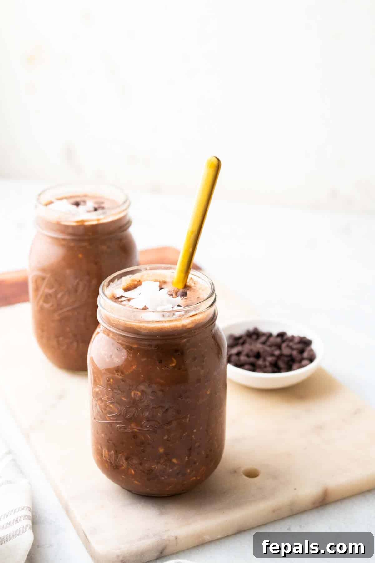 Two jars of chocolate peanut butter overnight oats, garnished with toppings and a spoon in one