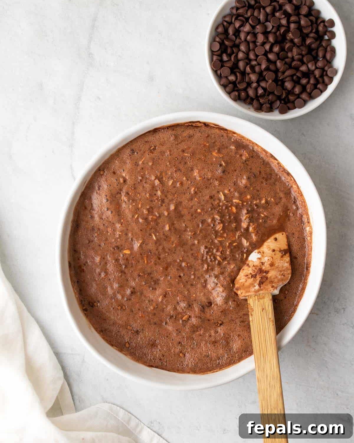 A spoon mixing the overnight oats ingredients in a bowl before adding chocolate chips
