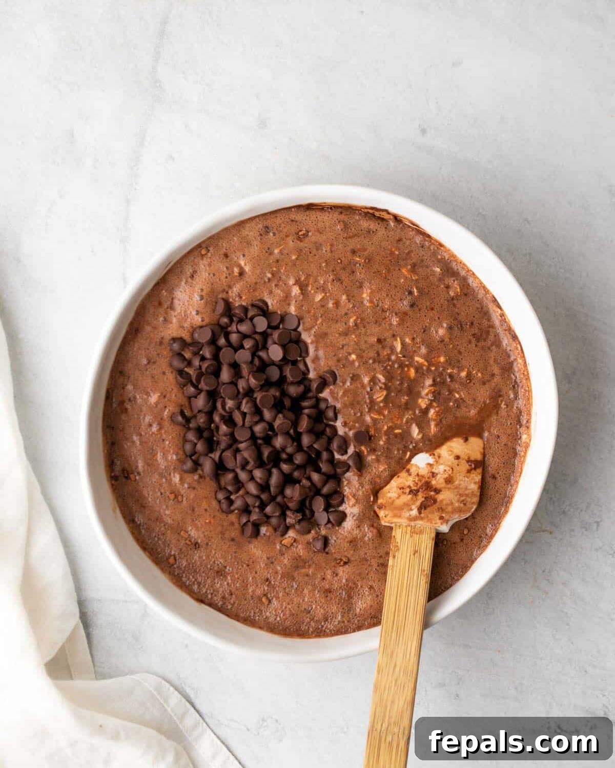 A spoon mixing chocolate chips into the chocolate peanut butter overnight oats mixture in a bowl