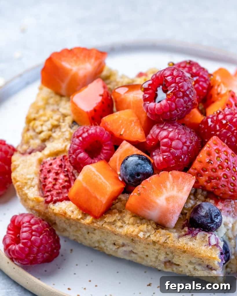 A close-up, inviting side view of a slice of baked oatmeal, generously topped with an assortment of fresh berries, resting on a white plate, ready to be savored.