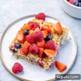 A delicious side shot of a slice of baked oatmeal on a white plate, beautifully topped with fresh berries and a drizzle of maple syrup, capturing its inviting texture.