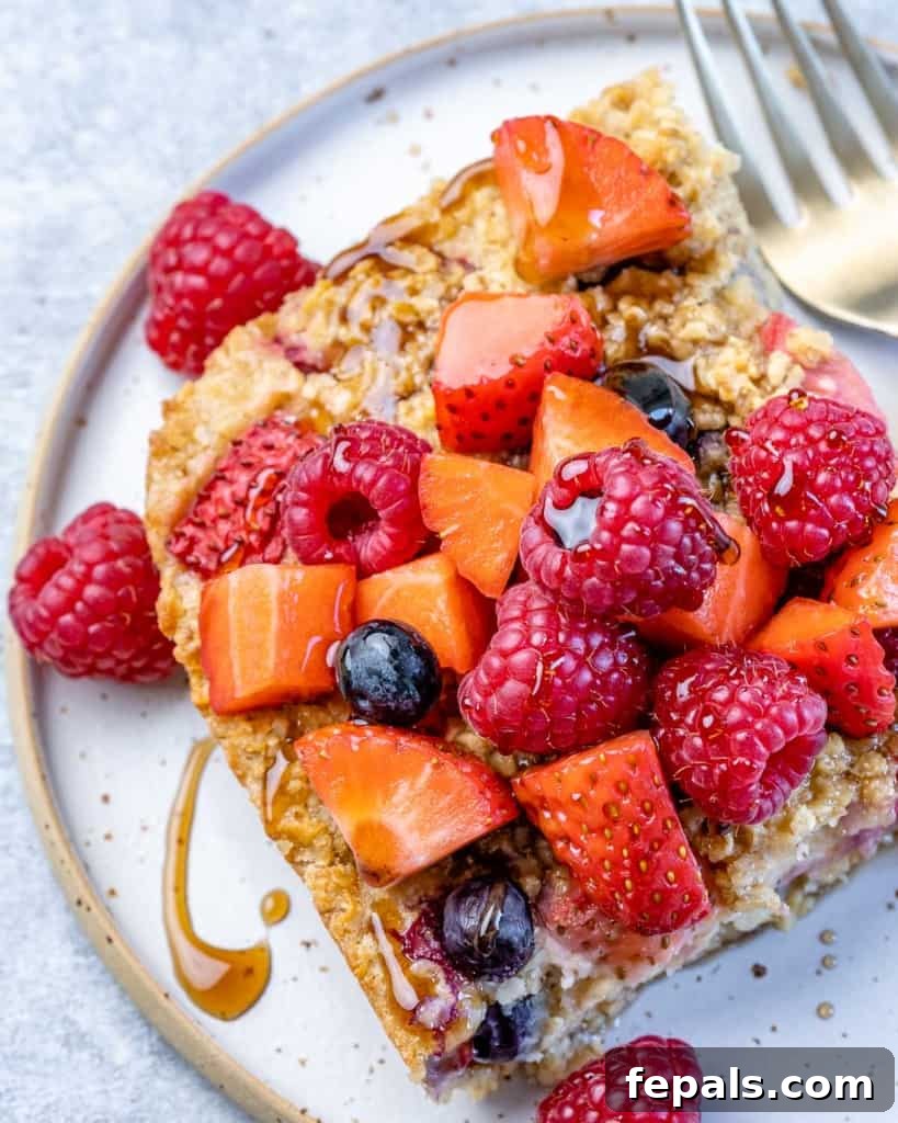A stunning top-down view of a golden-brown slice of baked oatmeal, adorned with a vibrant medley of fresh berries and a luscious drizzle of maple syrup, placed on a pristine white plate.