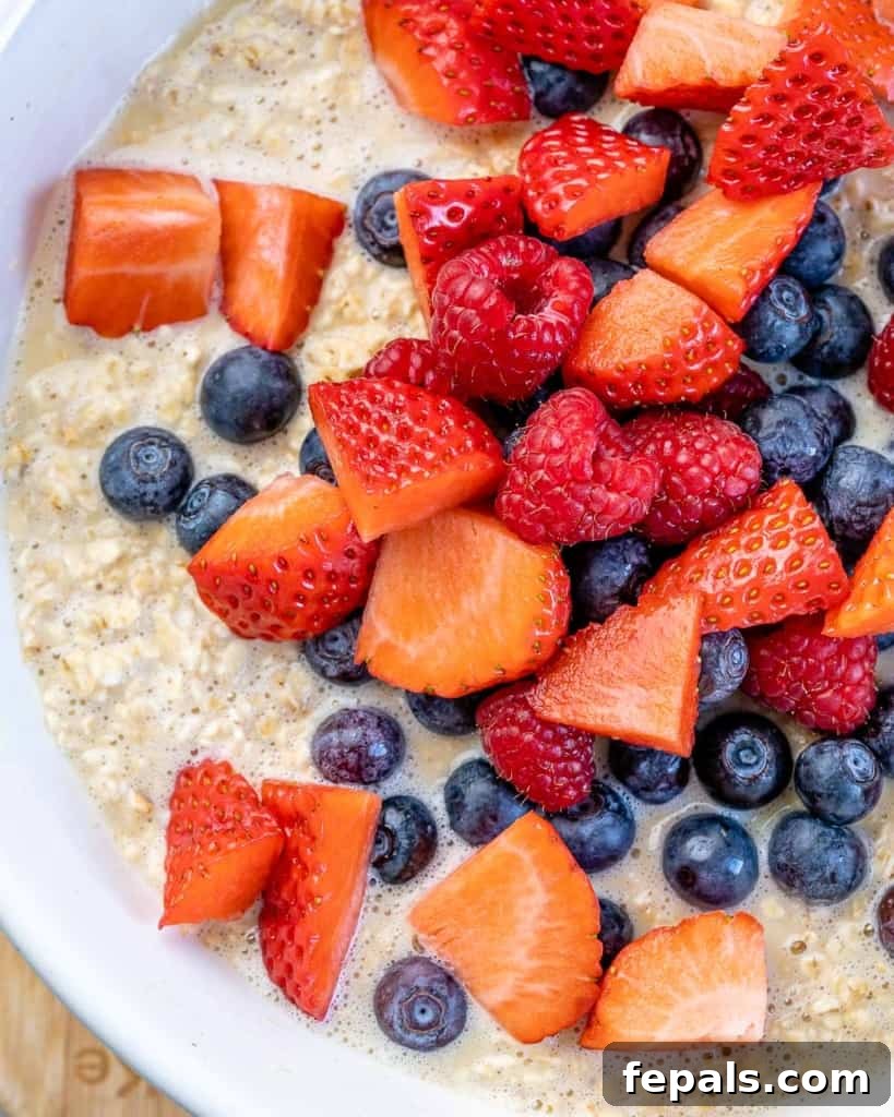 A close-up shot of the oatmeal mixture in a mixing bowl, vibrant with an abundance of fresh mixed berries folded into the batter, ready to be transferred for baking.