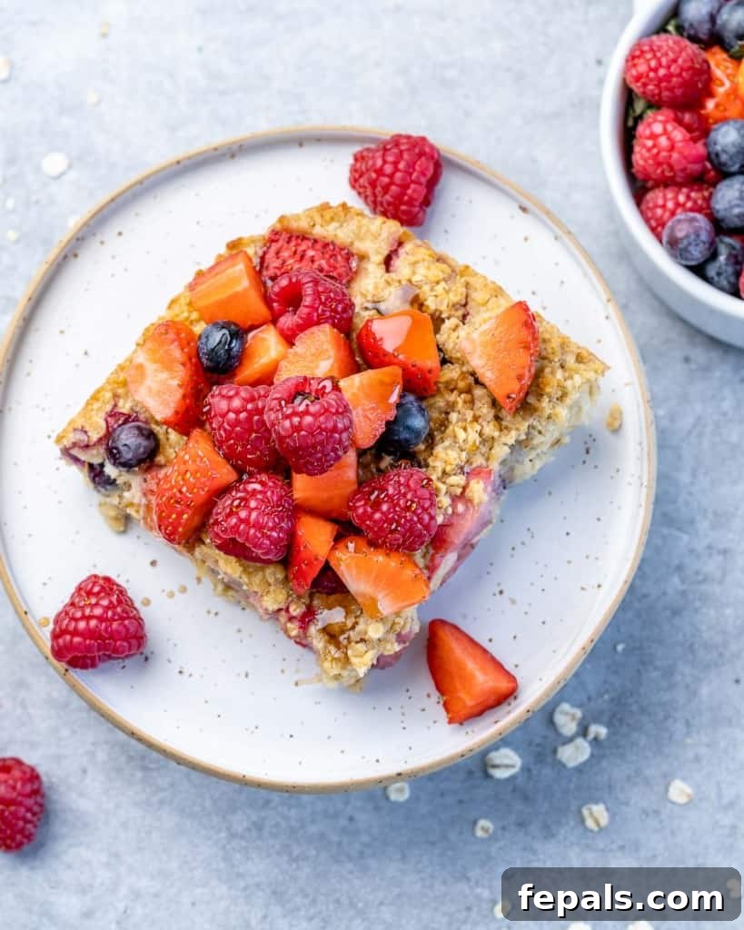 A perfectly portioned slice of baked oatmeal, delicately placed on a pristine white plate, showcasing its fluffy texture and the rich berry topping.