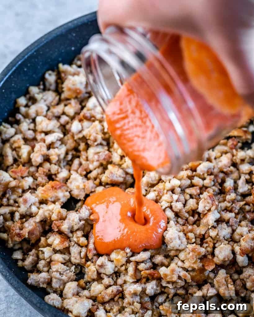Adding buffalo sauce to ground chicken in a black pan.