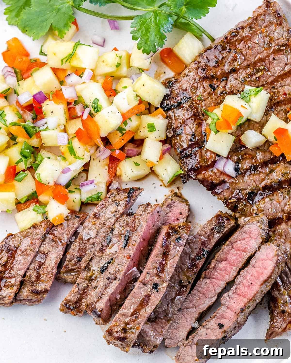 Perfect Grilled Skirt Steak with Pineapple Salsa Recipe side view of flank steak recipe on white plate with pineapple salsa and cilantro