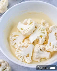 cauliflower floret in the buttermilk mixture in a white bowl