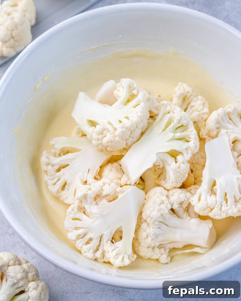 Cauliflower being added to a white bowl of buttermilk sauce.