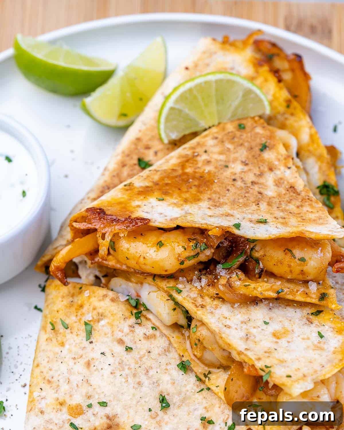 Easy Seafood Quesadillas Ready to Eat Front view of golden-brown shrimp quesadillas on a white plate, served with a side of sour cream and fresh lime wedges.