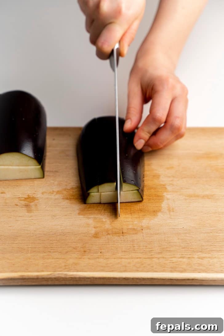 Initial Dicing of Eggplant Planks Dicing an eggplant into smaller sections after initial lengthwise cuts.
