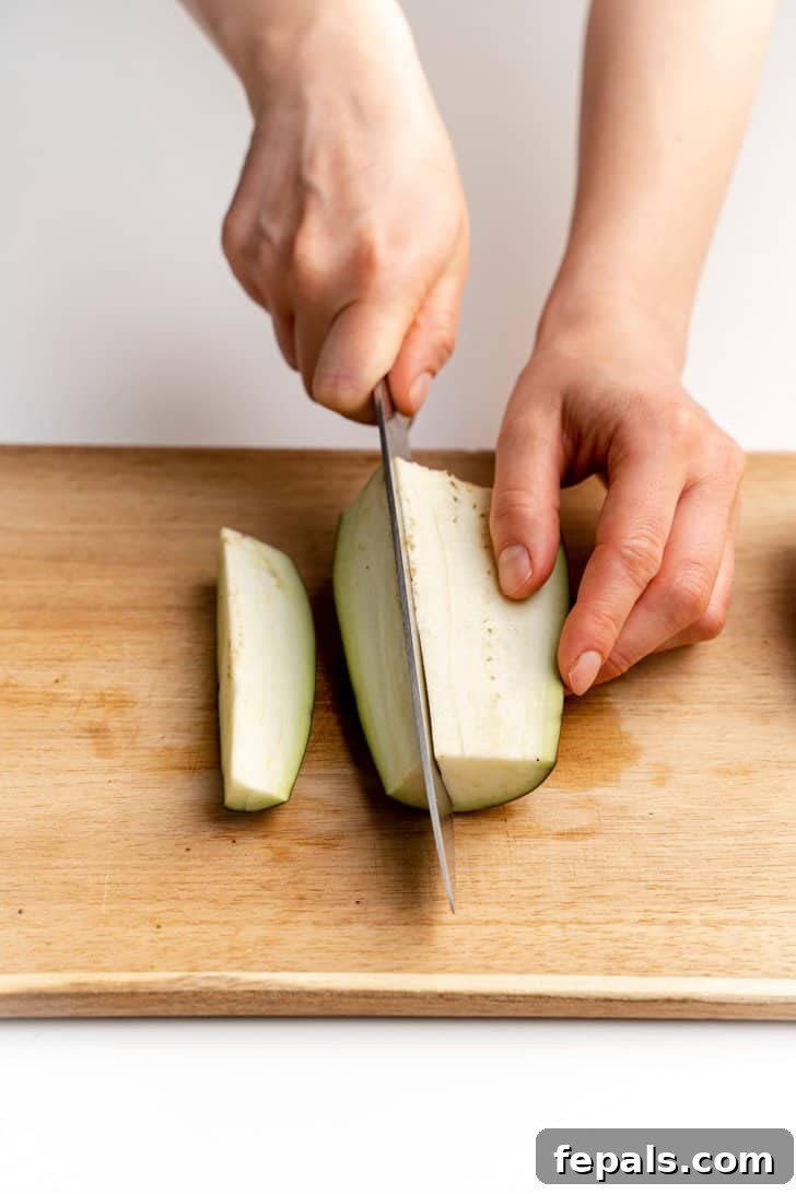 Slicing Eggplant into Long Strips A knife expertly cutting an eggplant into long, even strips.