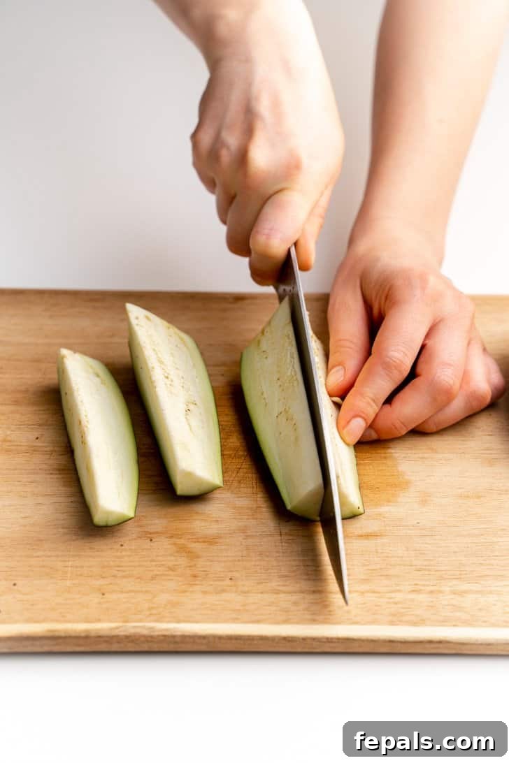 Uniform Eggplant Strips for Cooking Close-up view of the eggplant being sliced lengthwise into thin, uniform strips.