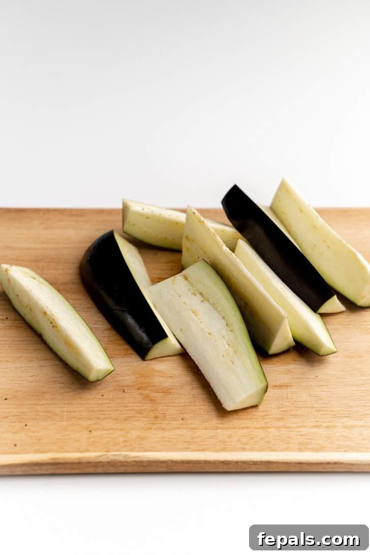 Three Different Eggplant Cuts for Diverse Recipes A cutting board displaying various cuts of eggplant: rounds, cubes, and long strips.