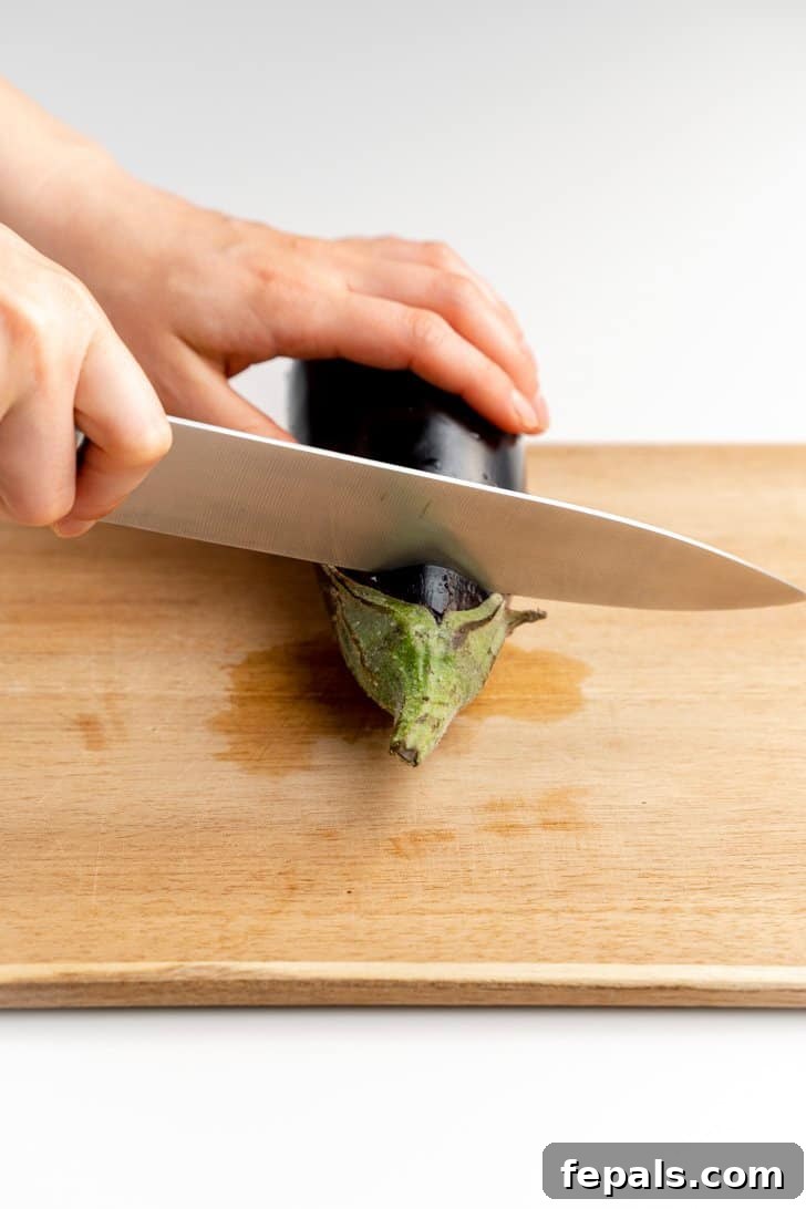 Preparing Eggplant by Removing the Stem Slicing the stem off the top of an eggplant to prepare it for cutting.
